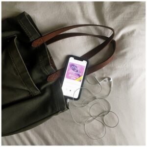cell phone with audiobook displayed on bed with purse